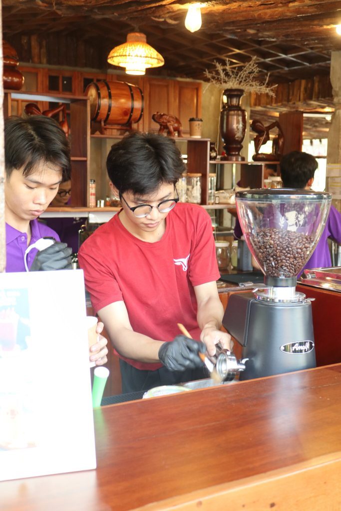 Barista True Cafe áo đỏ thao tác trên máy pha tại quầy gỗ trong sự kiện ngoài trời
