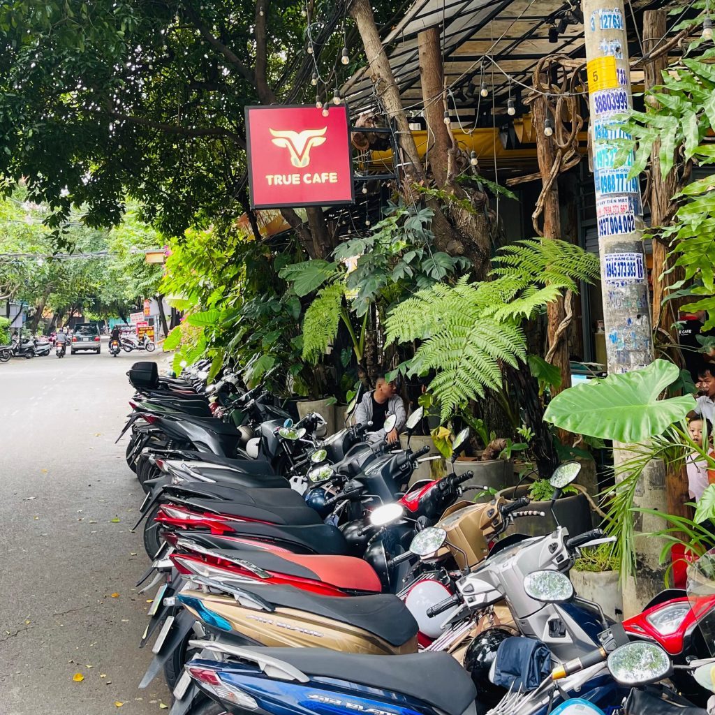 Biển hiệu True Cafe màu đỏ trước quán, xe máy của khách đậu thành hàng dài