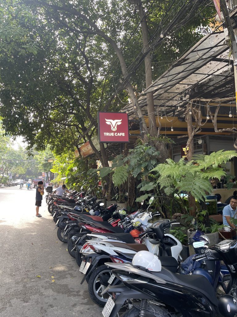 Biển hiệu True Cafe treo trước quán, hàng xe máy của khách đậu dài dọc vỉa hè