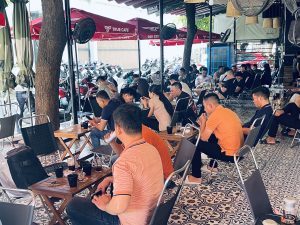 Khách ngồi kín các bàn dưới dàn dù đỏ in logo True Cafe, xe máy đậu dài phía sau