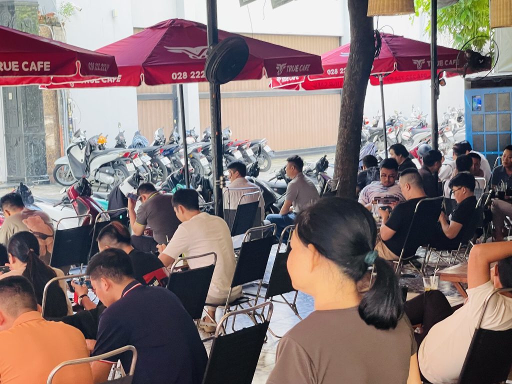 Khu ngồi ngoài trời dưới dù đỏ True Cafe với khách kín bàn vào buổi sáng