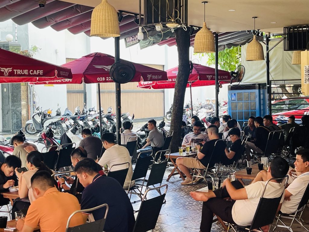 Toàn cảnh quán cà phê với dàn dù đỏ True Cafe và khách ngồi kín mọi bàn