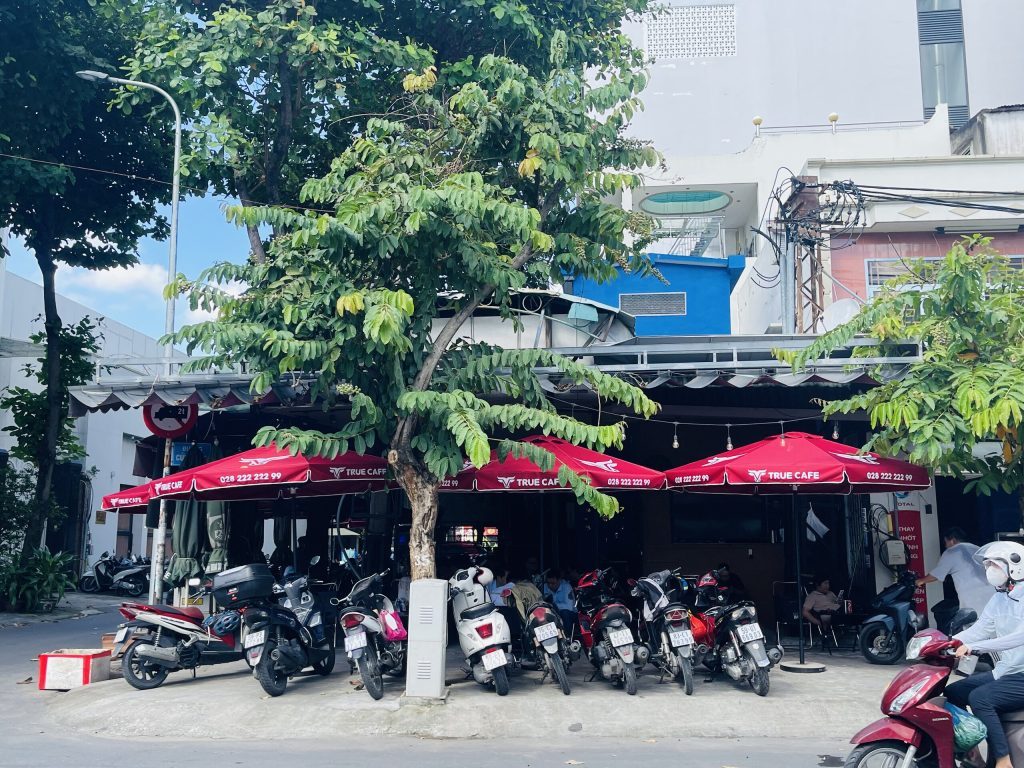 Mặt tiền quán cà phê với dãy dù đỏ in logo True Cafe và xe máy khách đậu kín