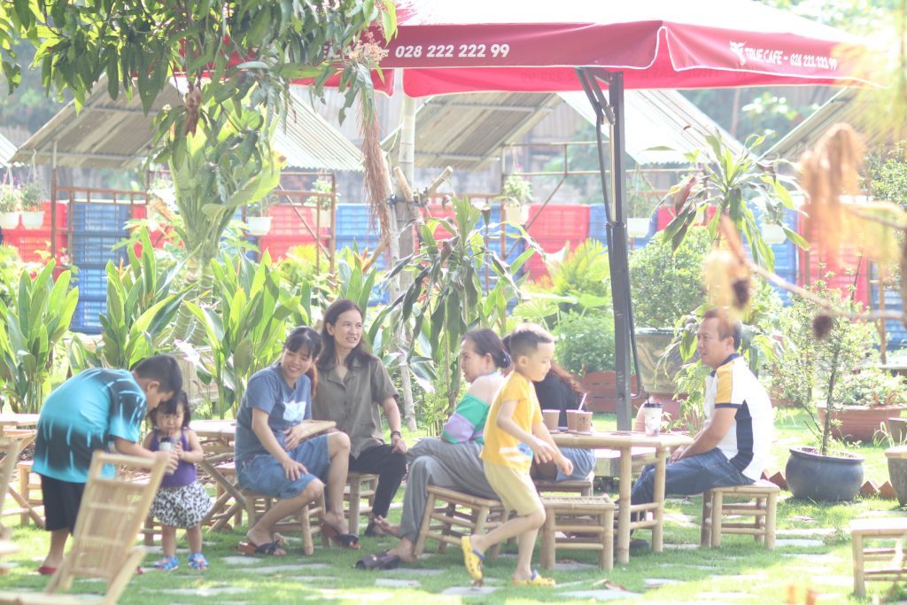 Gia đình ngồi trên khu sân cỏ dưới dù đỏ True Cafe tại quán cà phê sân vườn