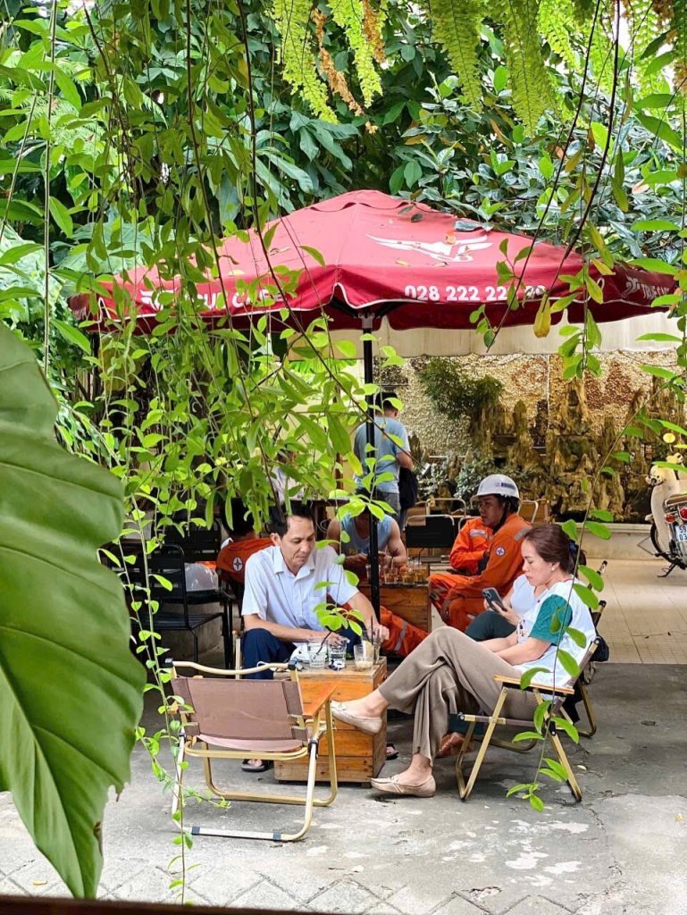 Khu ngồi sân vườn với dù đỏ True Cafe dưới giàn cây xanh, khách ngồi trò chuyện