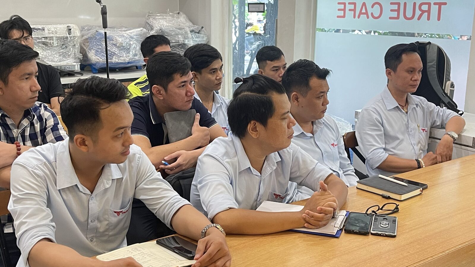 Phòng đào tạo True Cafe với vách kính in tên thương hiệu, chủ quán ngồi bàn dài trao đổi