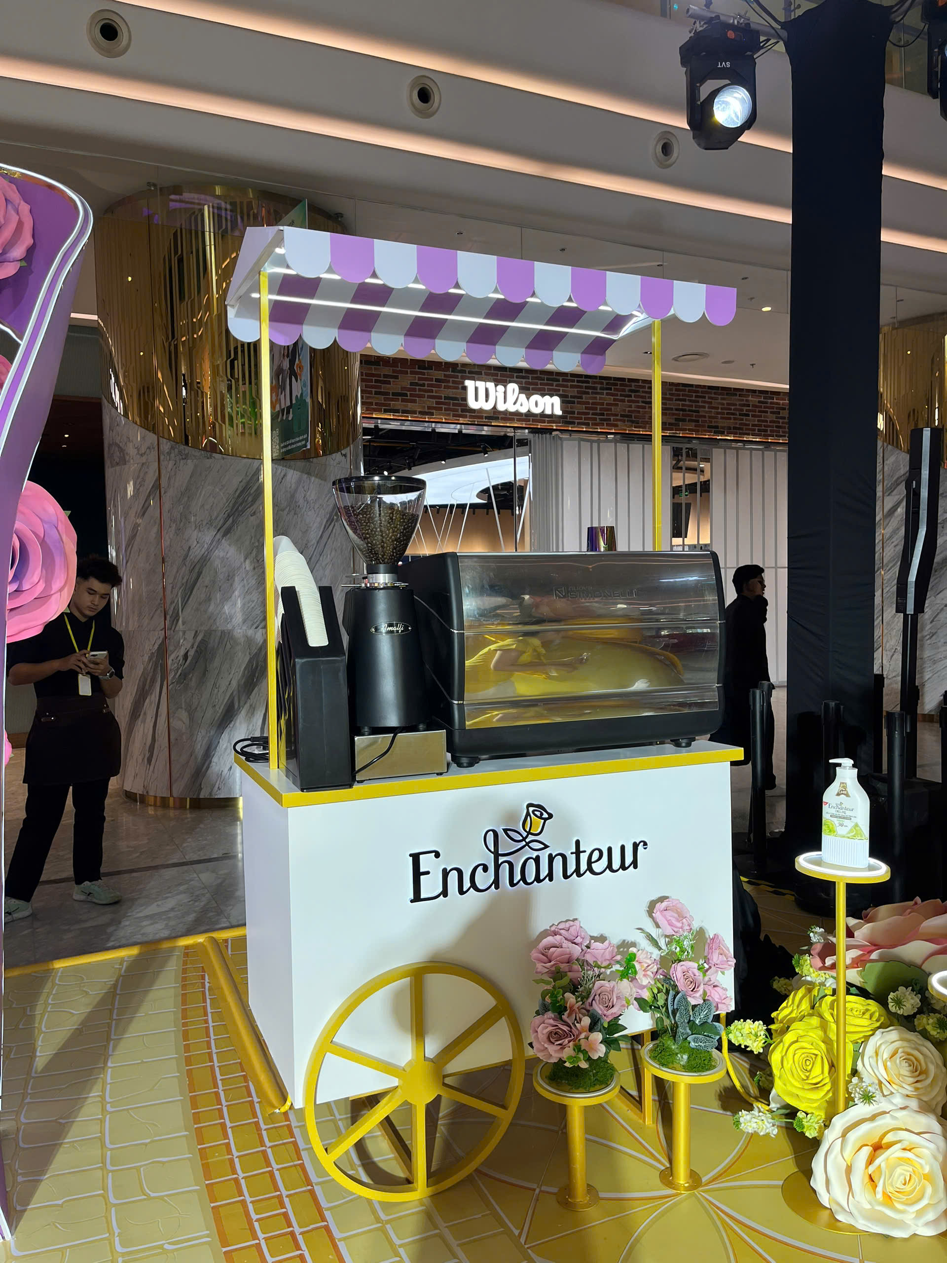 Quầy cà phê xe đẩy in logo Enchanteur với máy pha espresso và hoa trang trí tại sự kiện